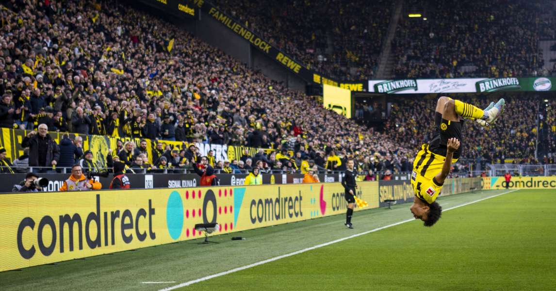 Borussia Dortmund player celebrates with a backflip as fans cheer and comdirect ads display on perimeter boards at Signal Iduna Park